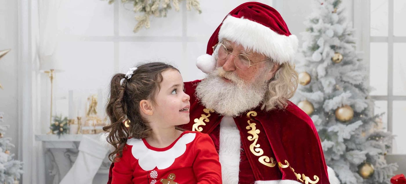 Santa smiling at a little girl in a red dress on his lap