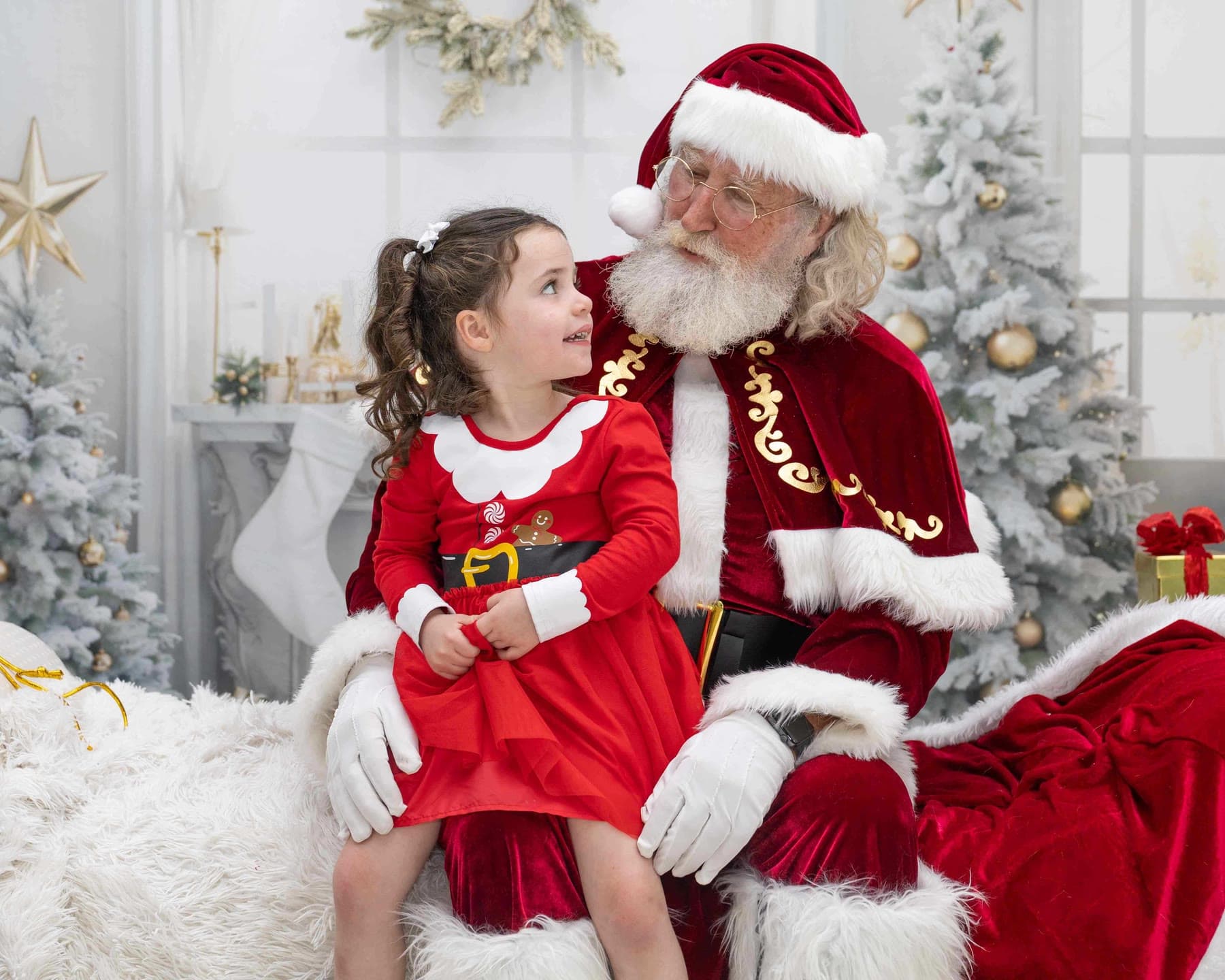 Santa smiling at a little girl in a red dress on his lap