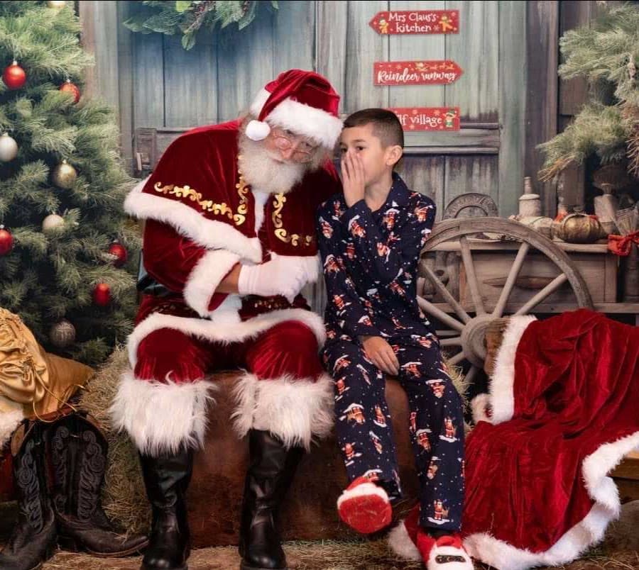 A boy in pajamas whispering his wish to Santa at a photo backdrop