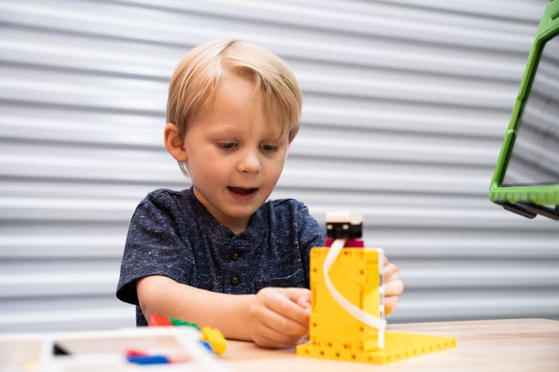 A boy winds the strap on a yellow brick machine