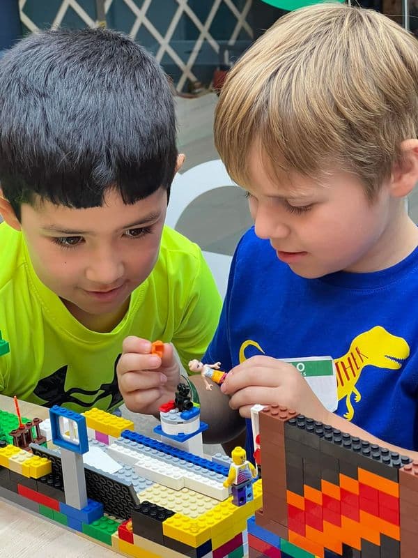Two boys lean over the brick town they are building together
