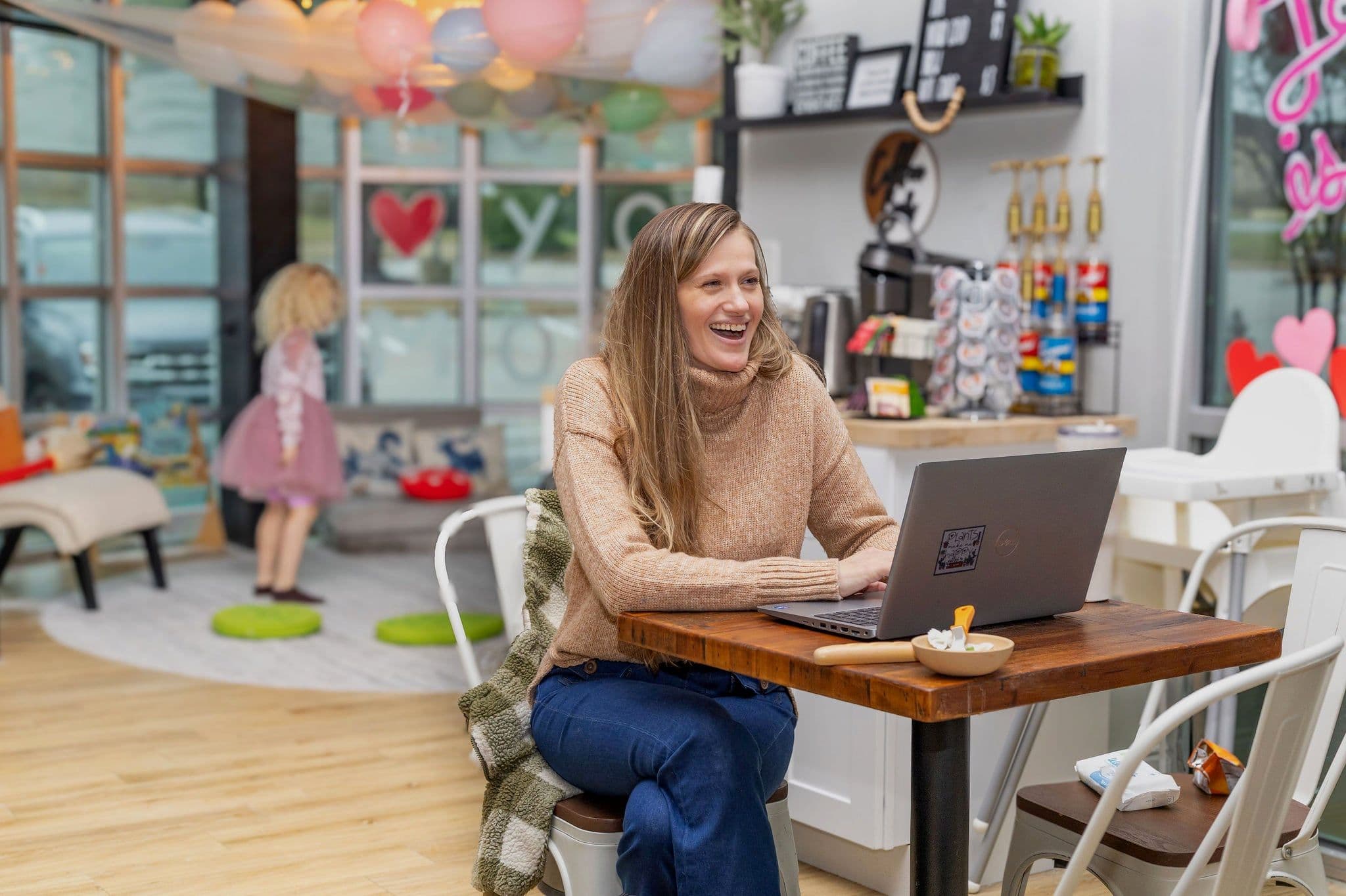 A mother laughing in the parent lounge while her daughter plays behind her