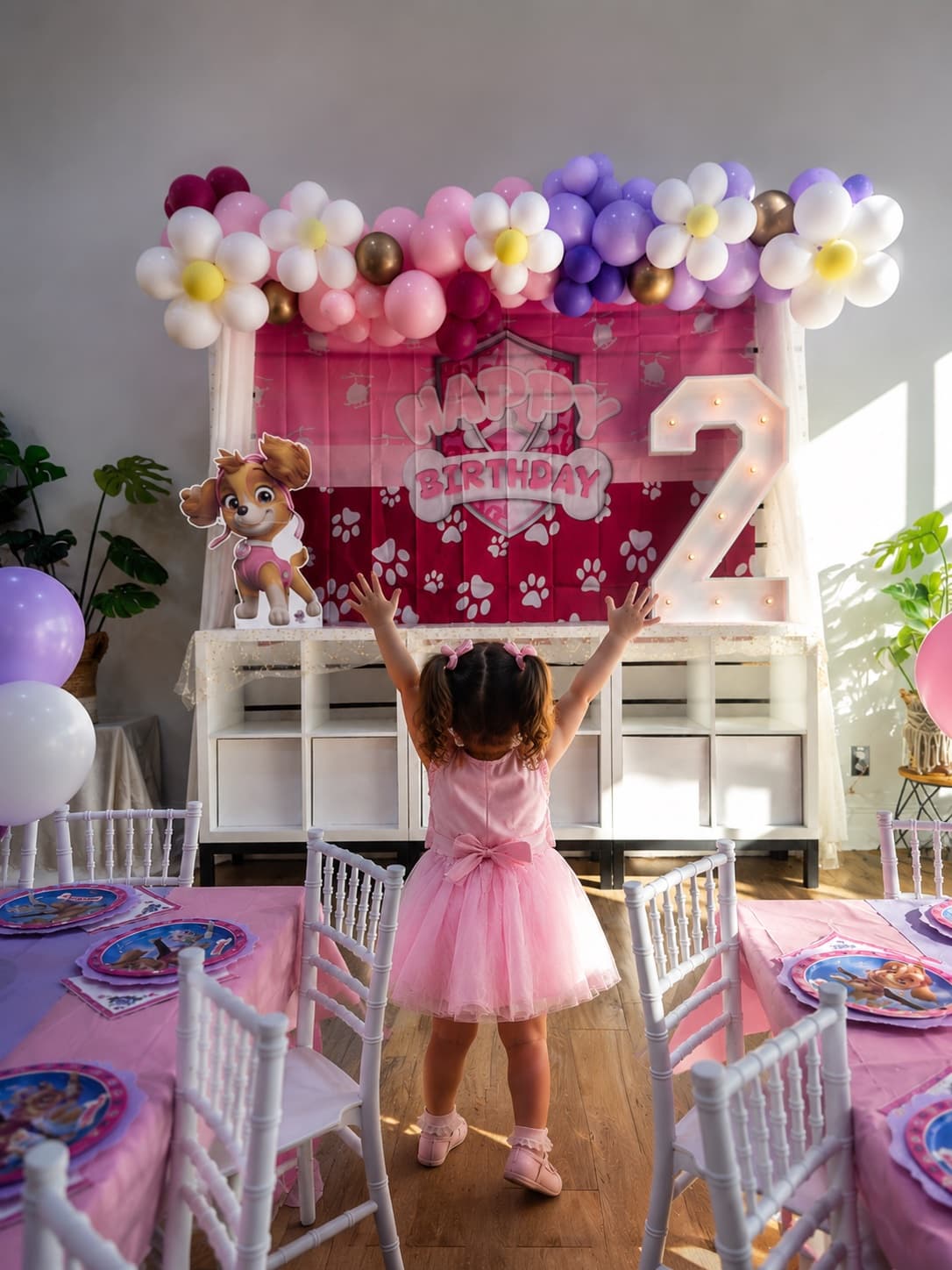 A little girl in a party dress in front of a fully decorated birthday backdrop at Pikopye's Town