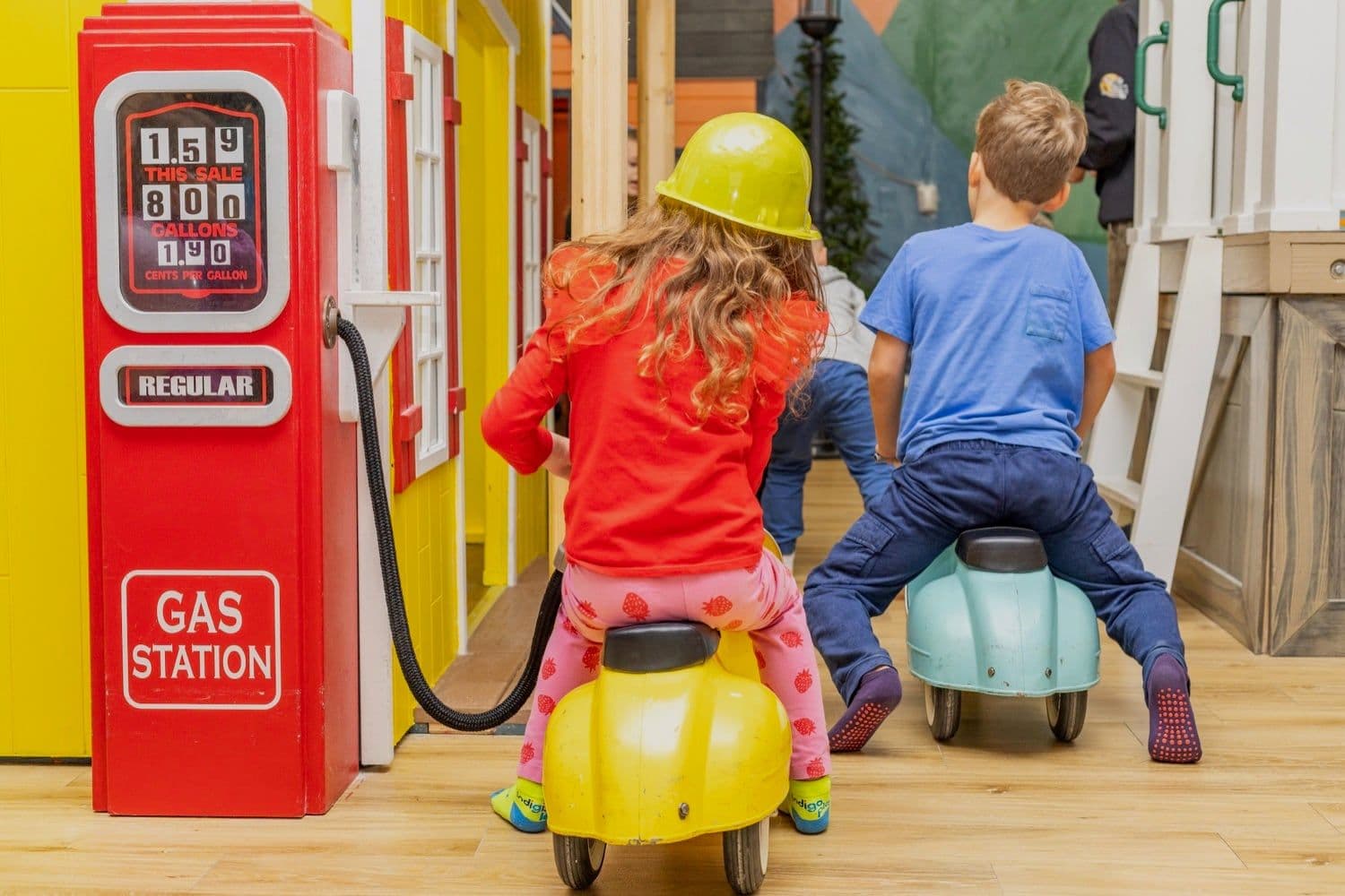 Two children on ride-on toys by the gas station playhouse during open play