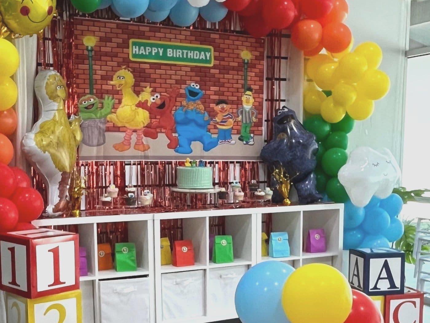 Brick street setup with a rainbow balloon arch, furry puppet characters and giant lettered blocks