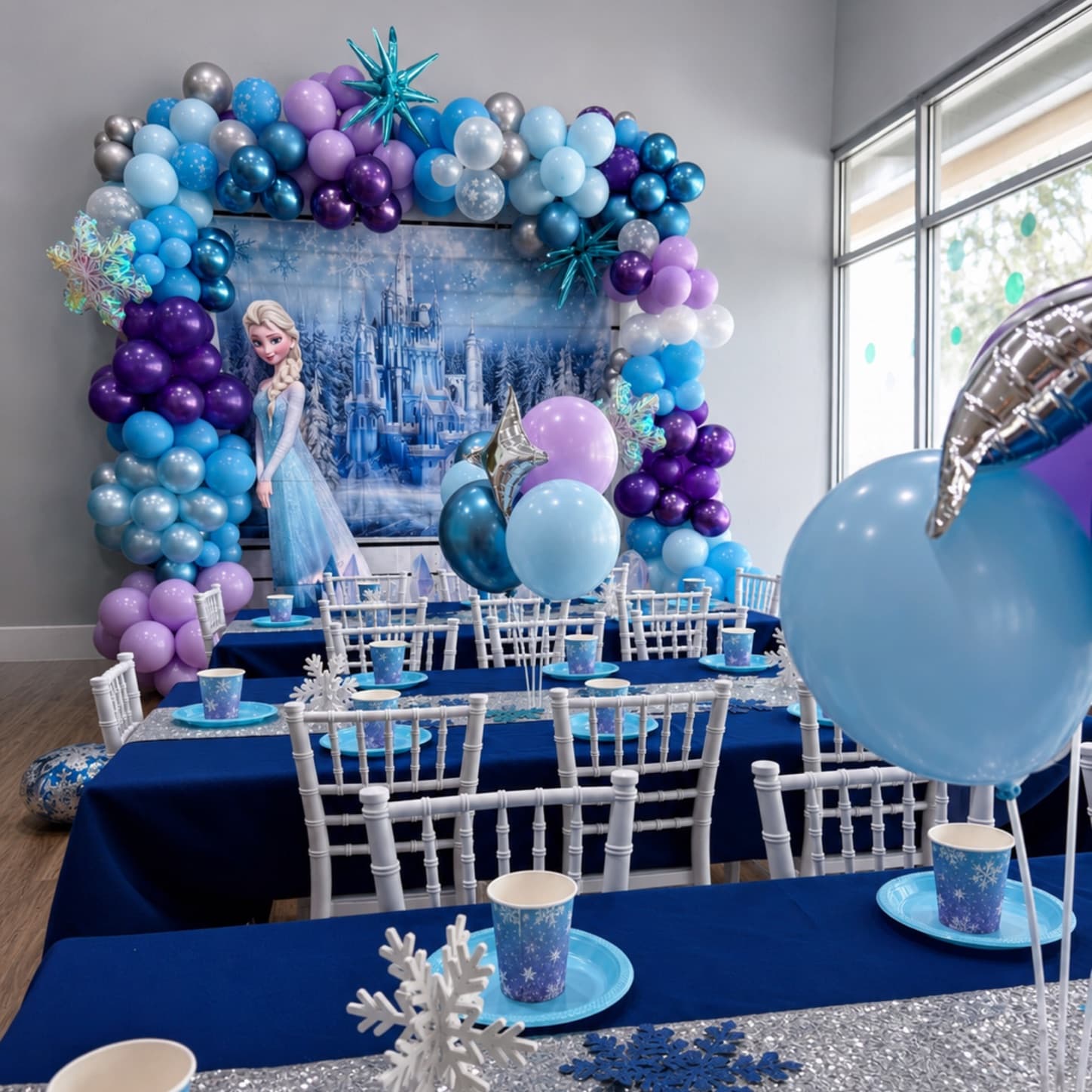 Ice princess birthday party setup with blue and purple balloon garland and snowflake tablescape