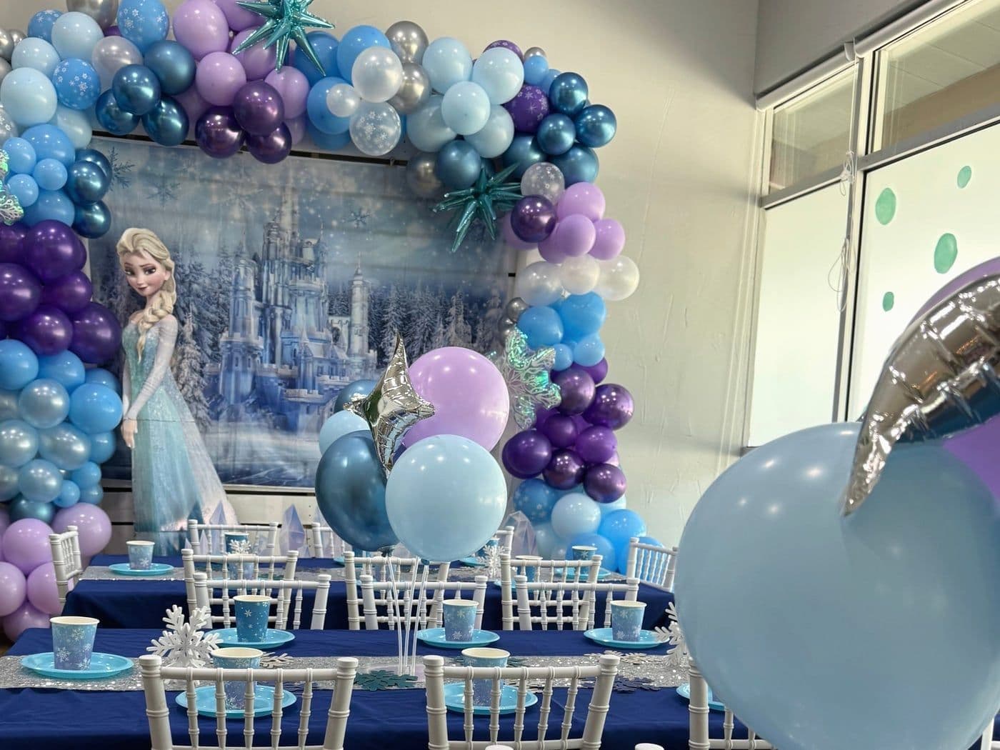Icy blue and purple setup with a snowflake balloon garland and a winter castle backdrop