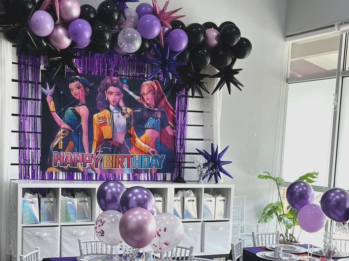 Black and purple pop star setup with a fringe curtain, starburst balloons and an animated girl group backdrop