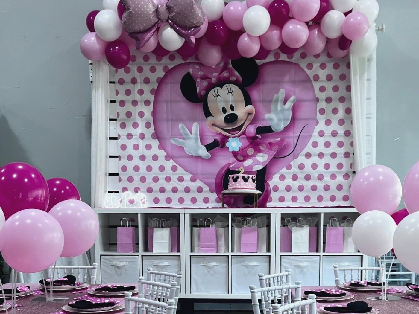 Pink polka dot setup with a bow balloon garland, a heart backdrop and favor bags in every cubby