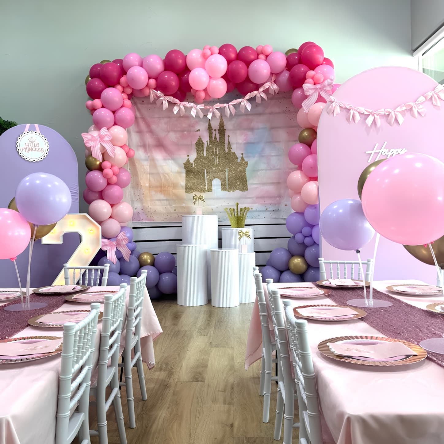 Pink princess birthday party setup with balloon arch, castle backdrop, and rose gold tablescape