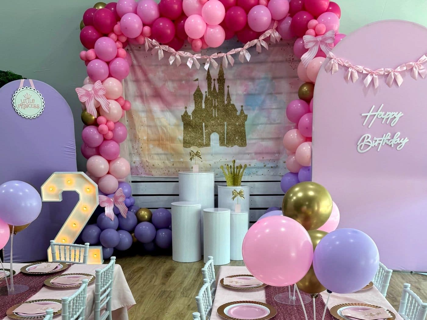 Pink and purple princess setup with a bow garland, a castle backdrop and a lit marquee number
