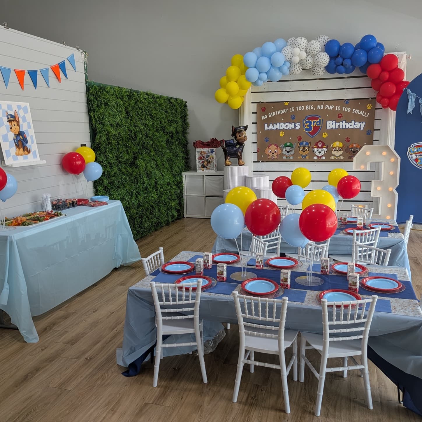 Rescue pup birthday party setup with a red, blue, and yellow balloon arch and a light-up number three