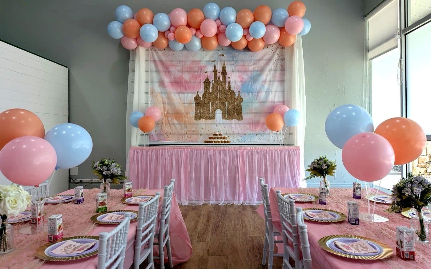 A styled party room: pastel balloon garland, a castle backdrop, a cupcake tower and laid tables, finished before guests arrive