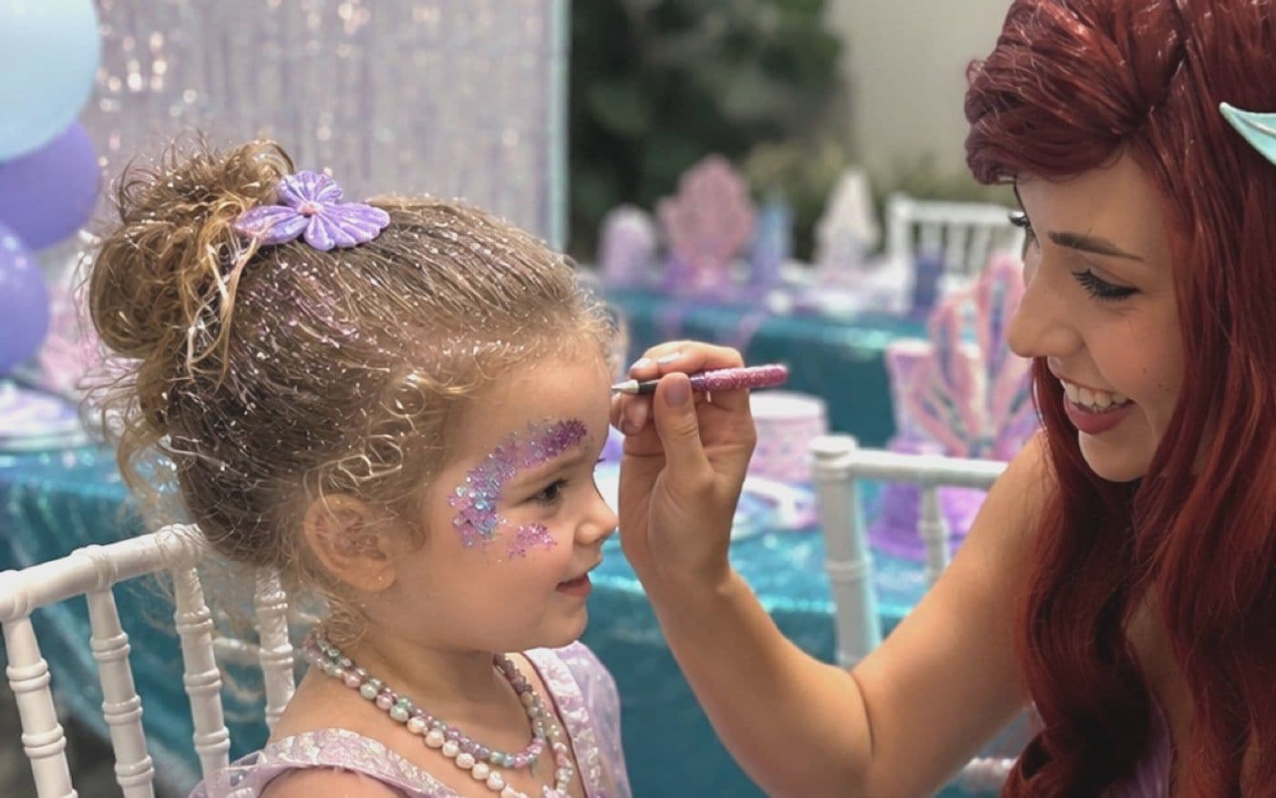 A host painting glitter onto a child's cheek at a laid party table